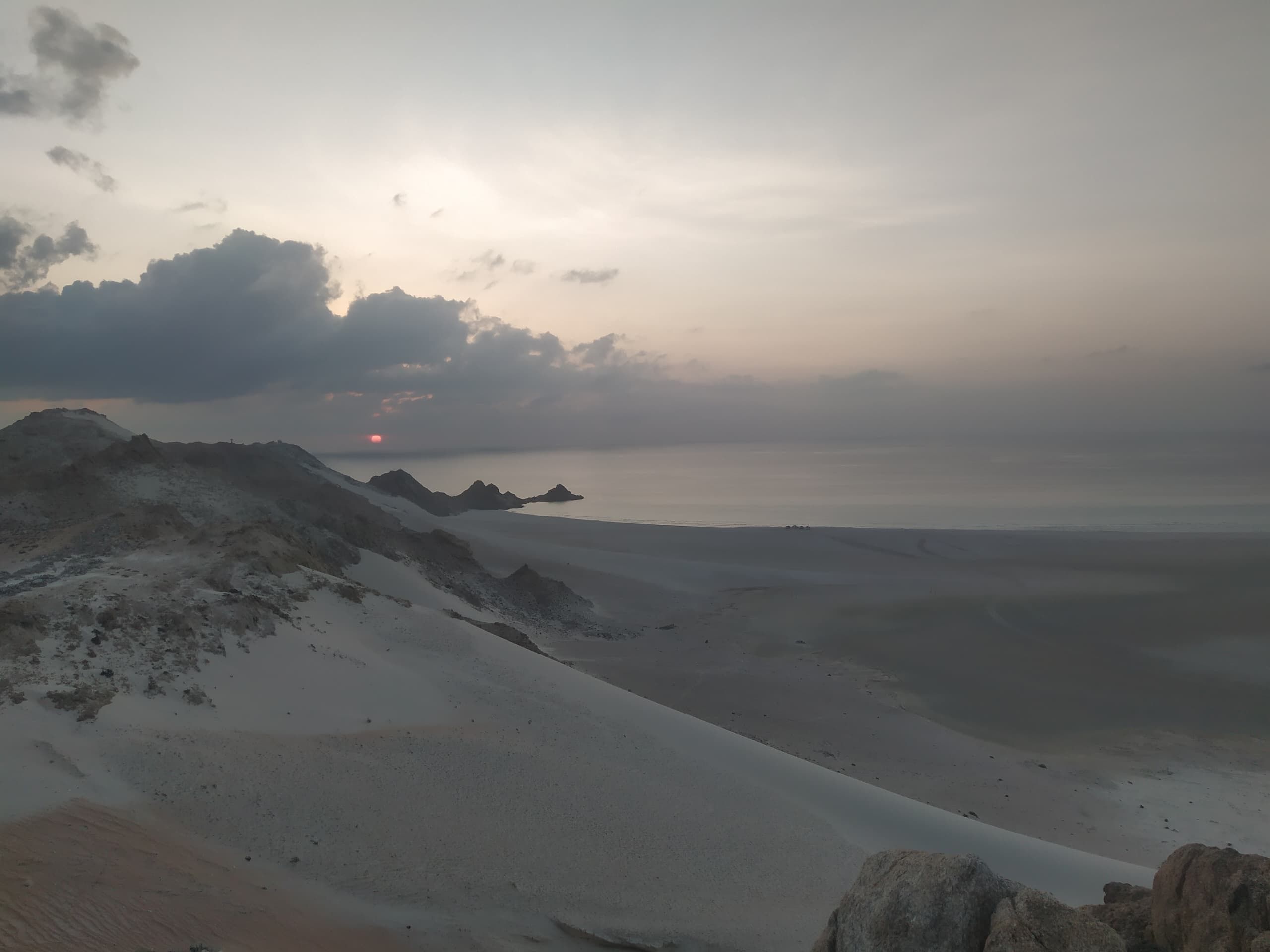A long dune ridge above the sea with the sun sitting low on the horizon