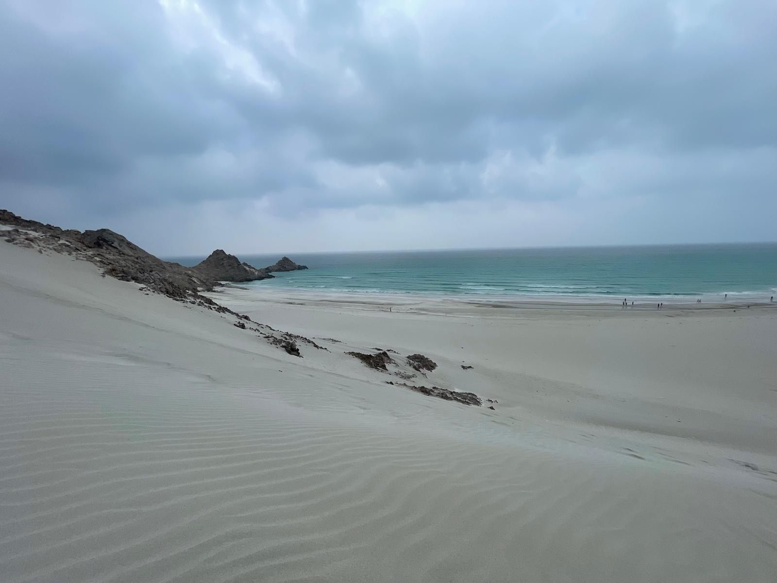 A rippled dune slope with dark rock outcrops under heavy cloud