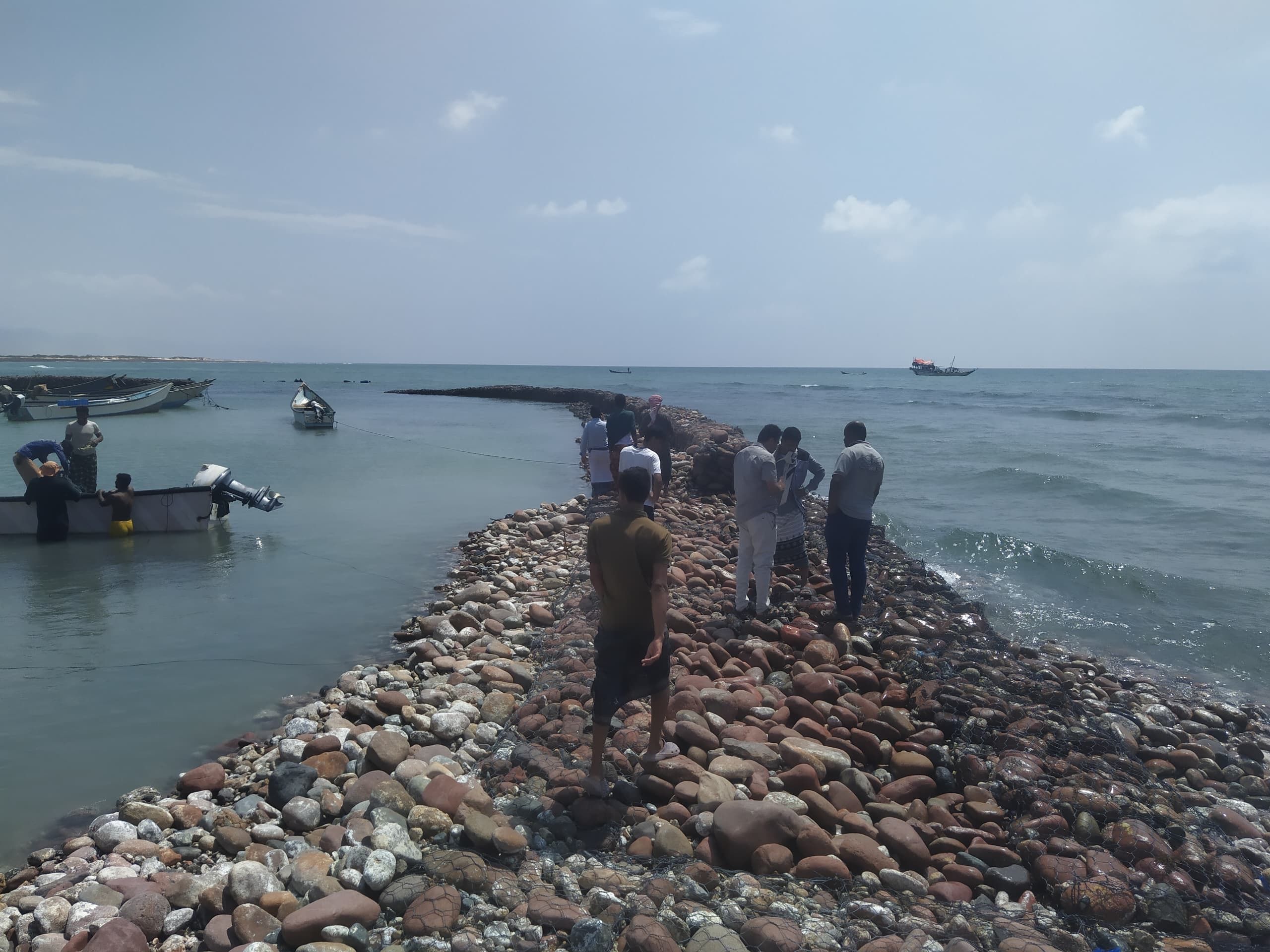 A group walking out along a stone causeway towards moored fishing boats