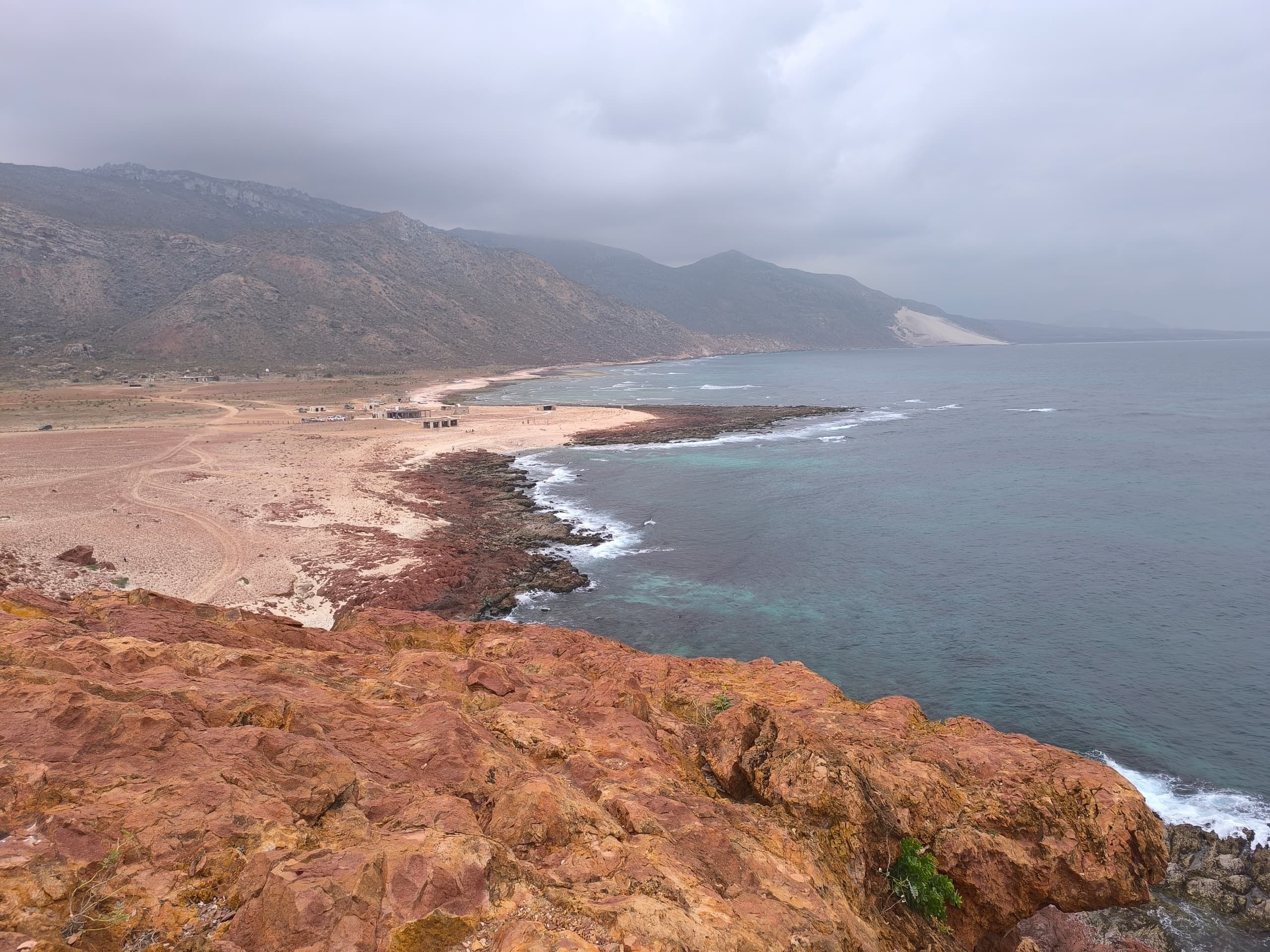A red rock headland dropping to a long curving bay of pale sand