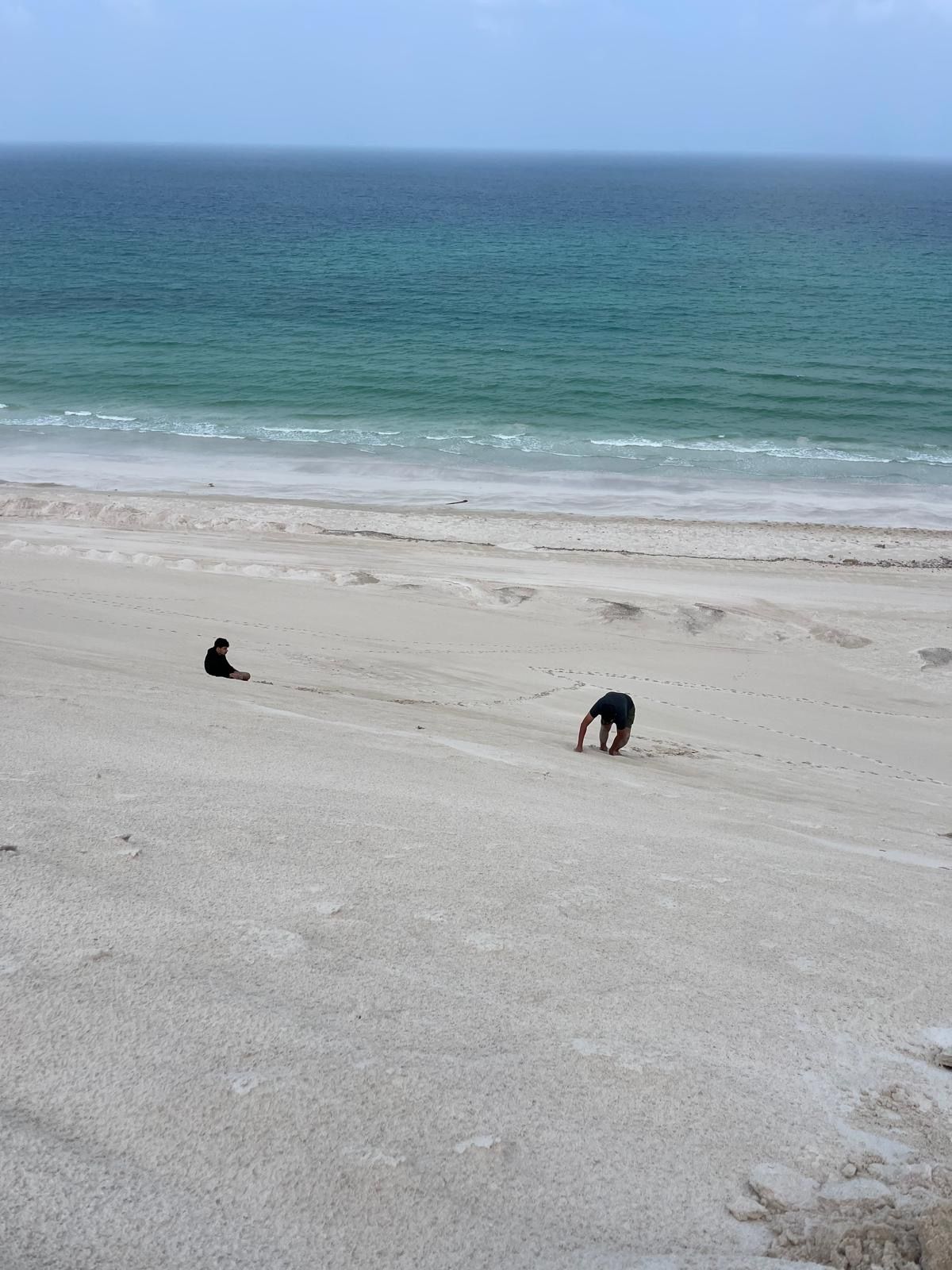 Two people making their way down a steep dune towards the sea