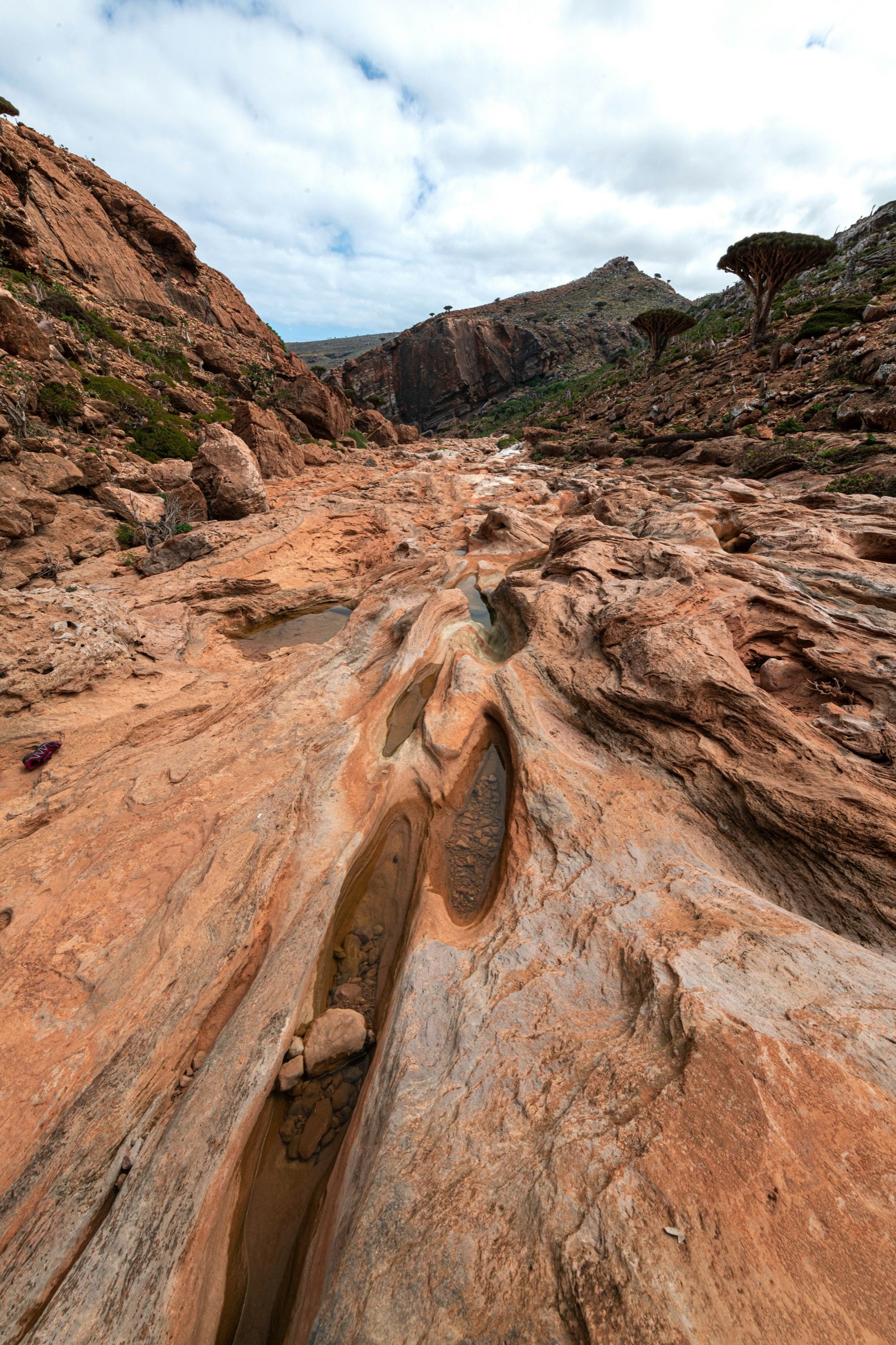 Water-carved channels and pools in orange sandstone beneath an overcast sky