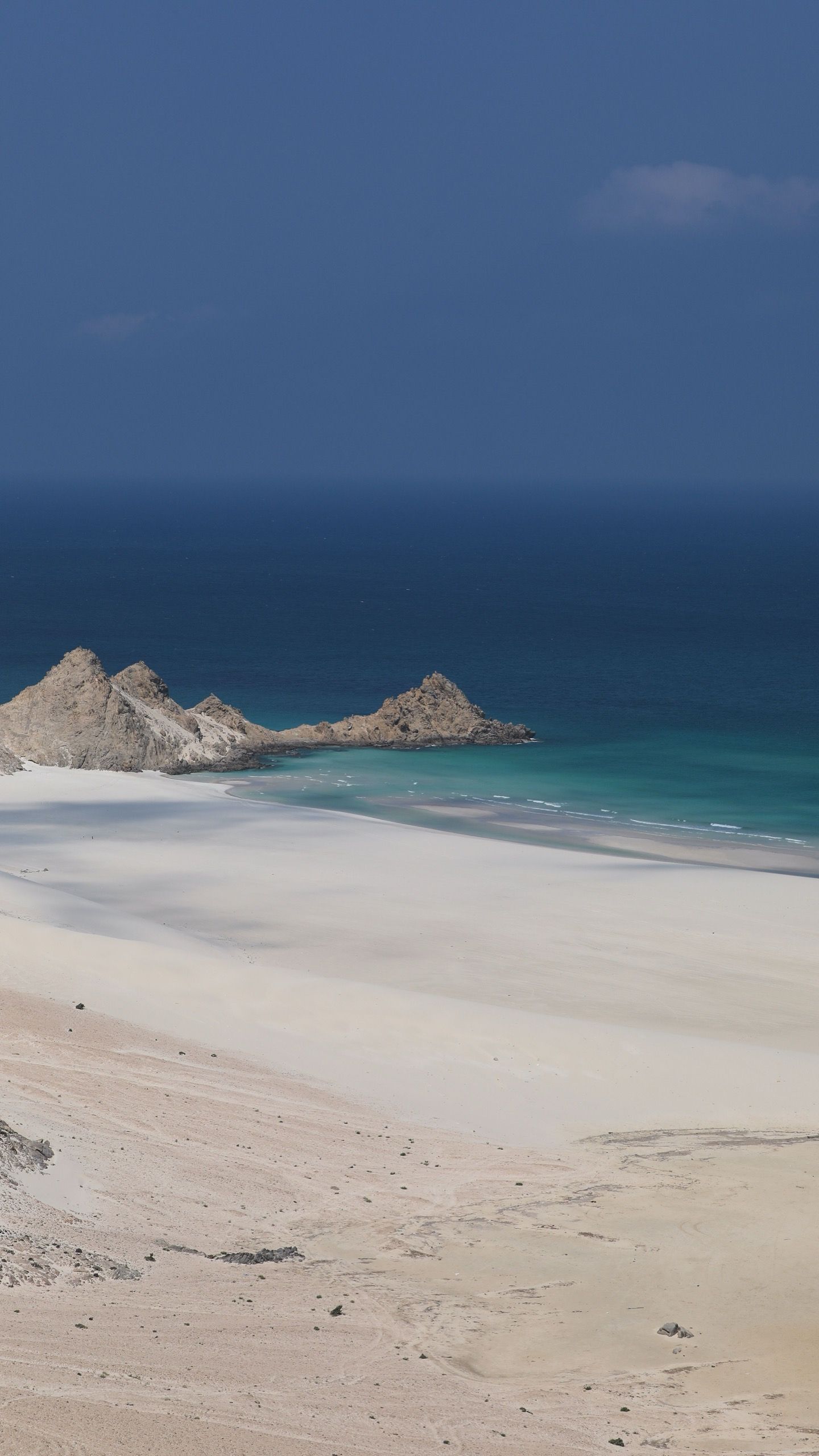 An empty white beach with rock outcrops standing in shallow turquoise water