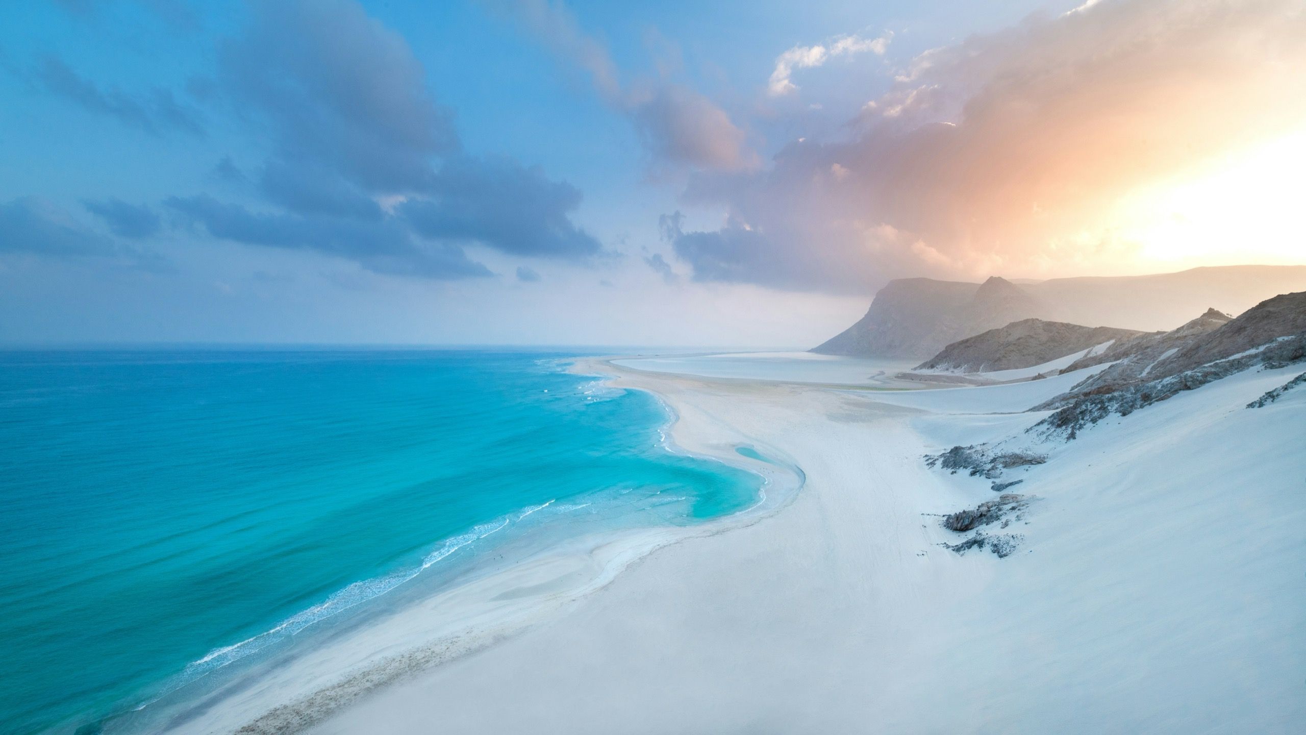 An elevated view of a long white sand spit with turquoise water curving in