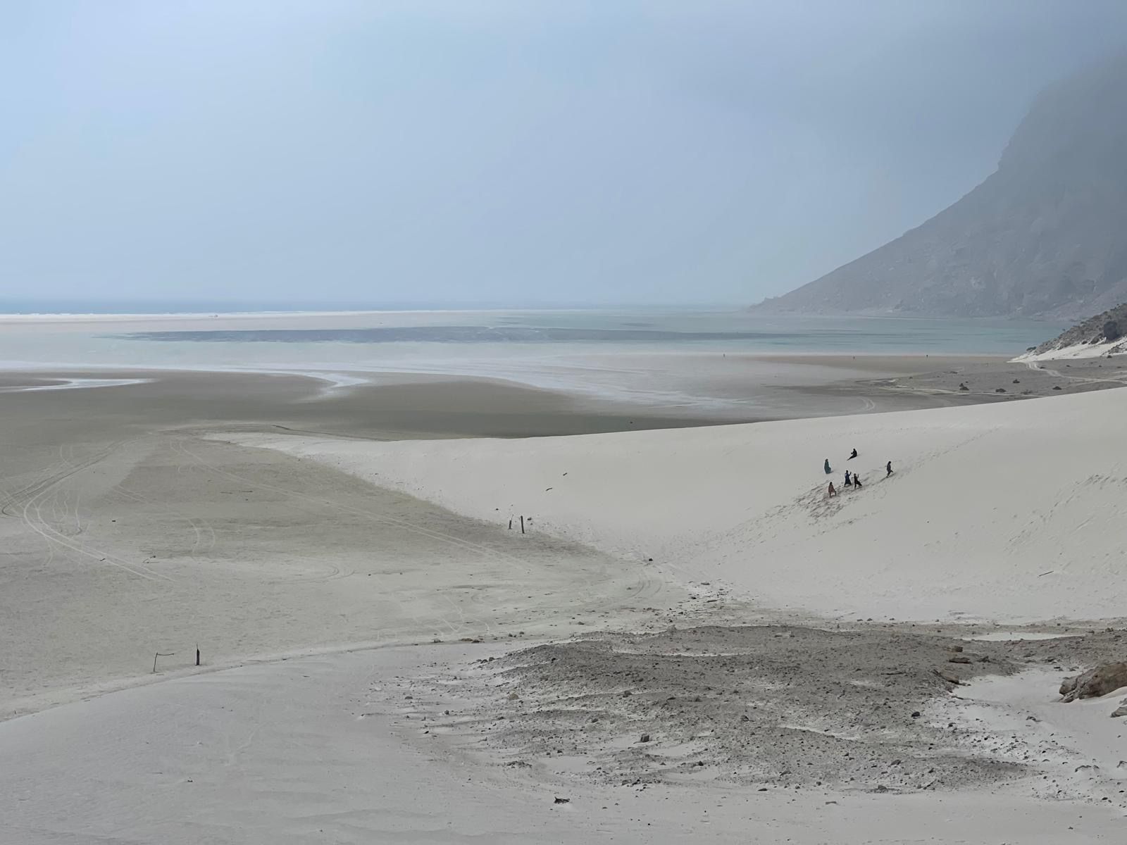 A vast pale dune sloping down to a shallow lagoon with a headland beyond