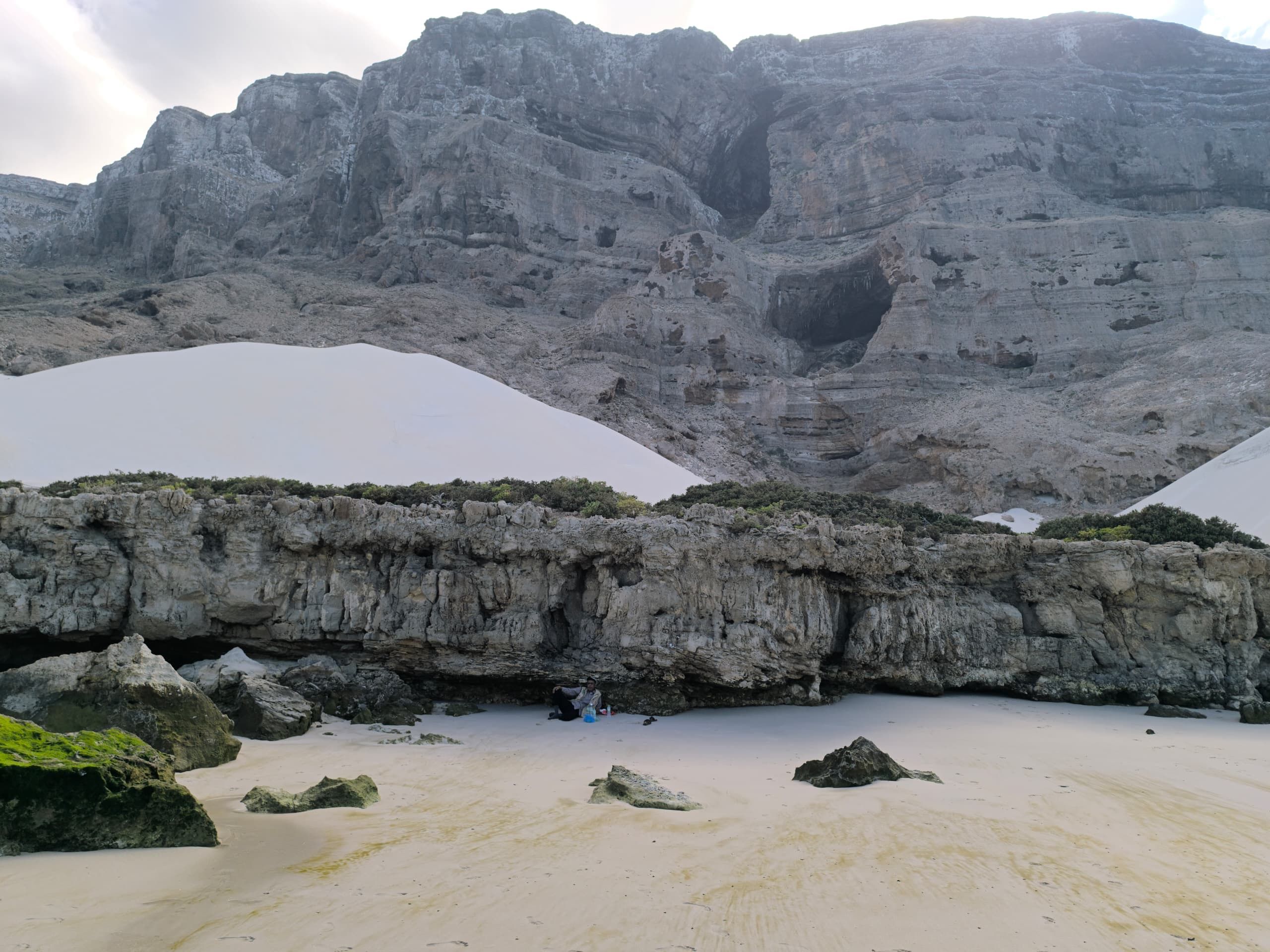 A white dune banked high against a sheer limestone cliff above a pale beach