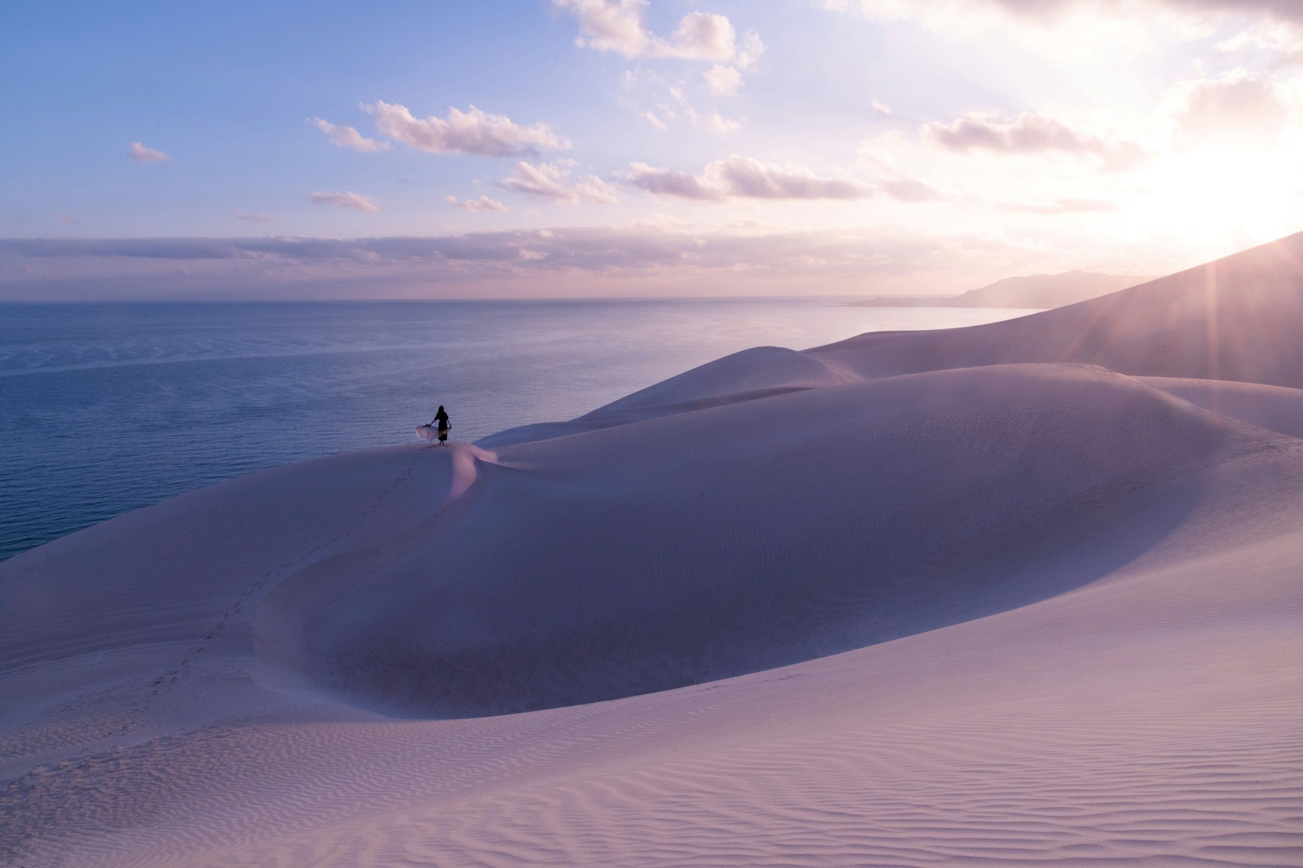 Pale dune ridges rising directly above the sea, with a single walking figure on the crest at dusk